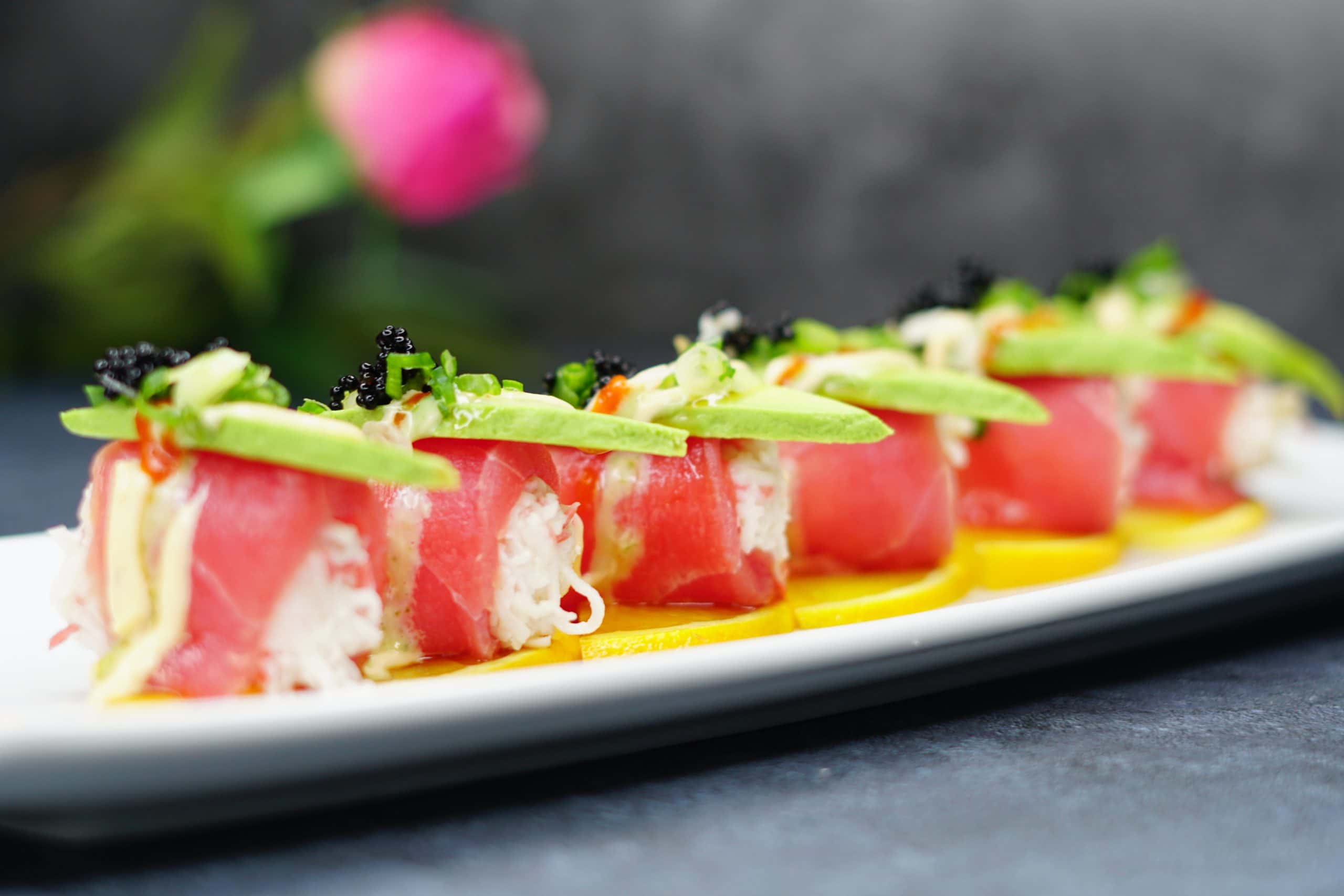 A rice-less roll wrapped in ruby-red tuna, topped with sliced avocado, black tobiko and micro greens, plated over mango